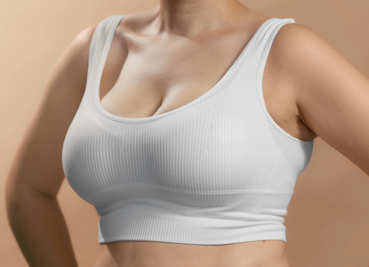 Caucasian woman in a white seamless bra and pink ribbon for breast cancer. Studio anonymous photo image on beige background.